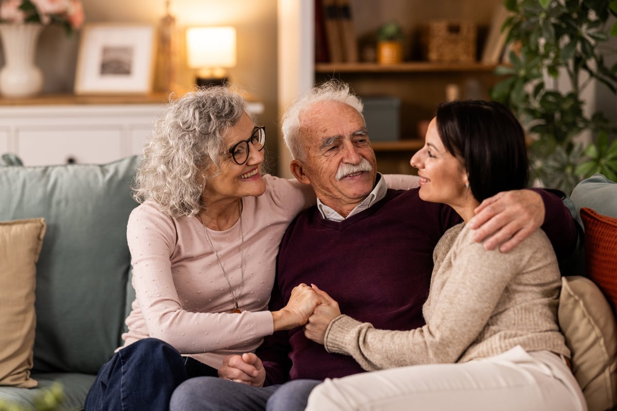 Daughter visiting and hugging her senior parents on the couch
